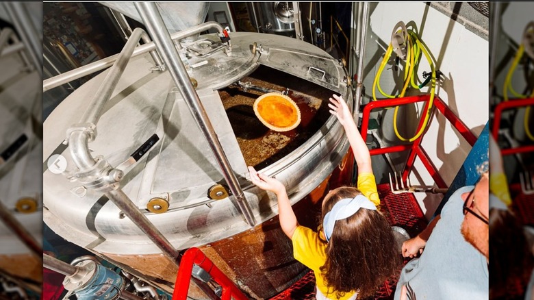 Child adding whole pumpkin pie to beer mash