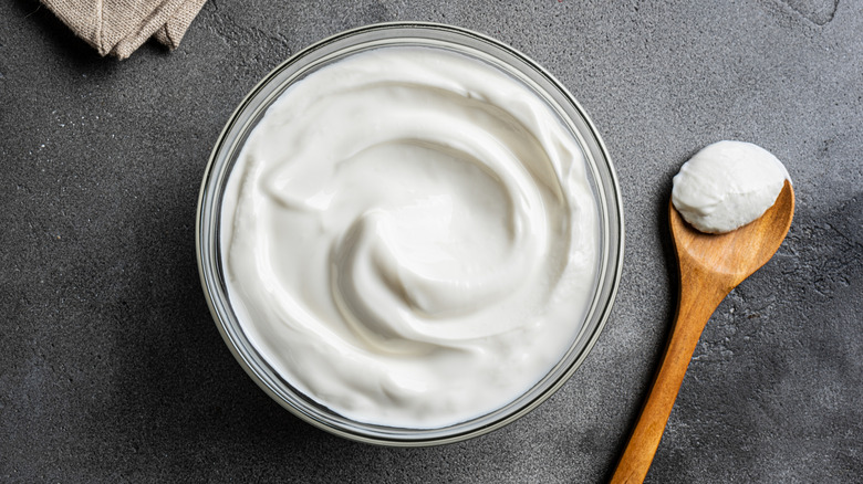 A bowl of Greek yogurt and a small wooden spoon of yogurt on a table
