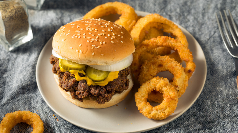 Homemade "slugburger," with pickles, raw onion and mustard, on a white plate with a side of onion rings