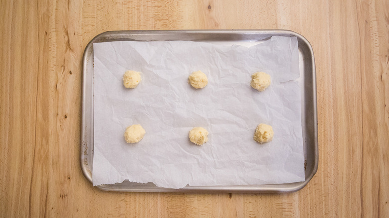 six dough balls sitting on lined cookie sheet