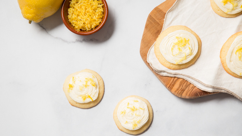 frosted lemonade cookies on table next to small bowl of lemon zest