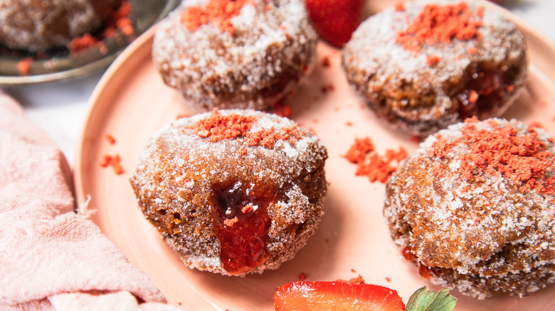 Four sugar-coated donuts on a pink plate with strawberries around them.