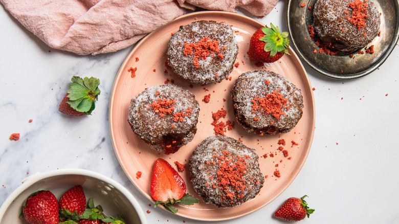 Overhead view of four sugar-coated donuts on a pink plate with strawberries around them.