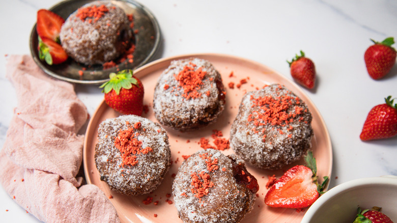 Five sugar-coated donuts on a pink plate with strawberries around them.