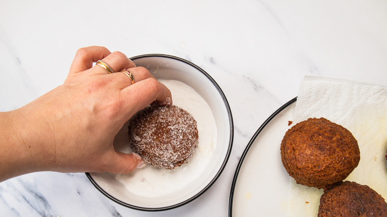 Rolling warm donut in sugar.