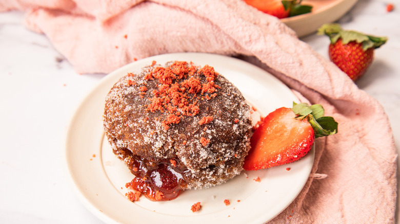 Single sugar-coated donut on a white plate with a sliced strawberry beside it.