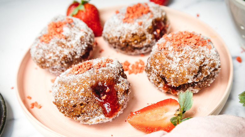 Four sugar-coated donuts on a pink plate with sliced strawberries.