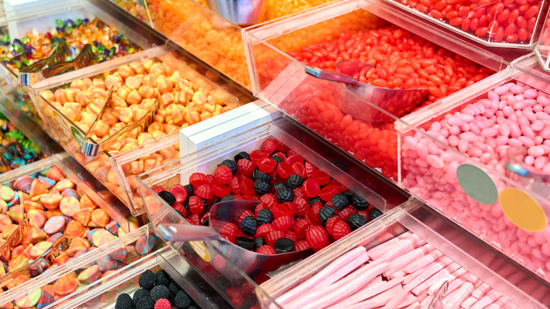Display of various gummy candies with scoops and tongs