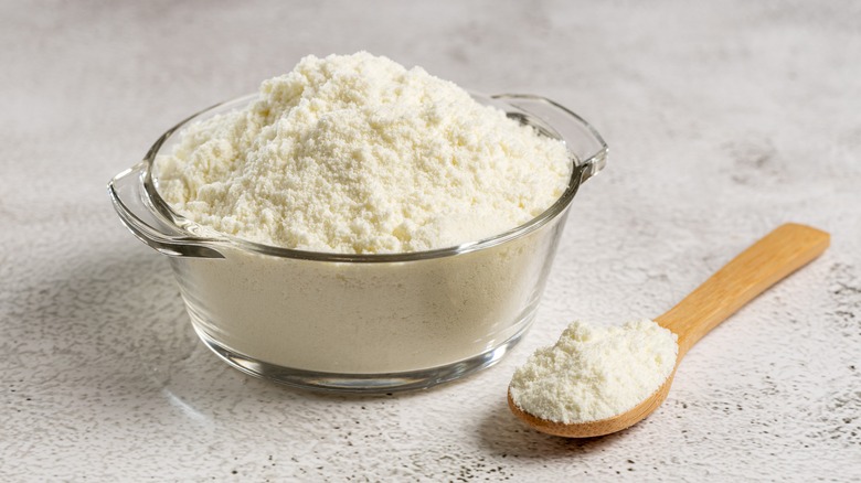 Powdered milk in a glass bowl next to a wooden spoon