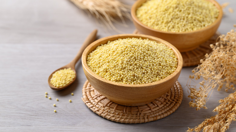 Dried millet in wooden bowls next to a wooden spoon