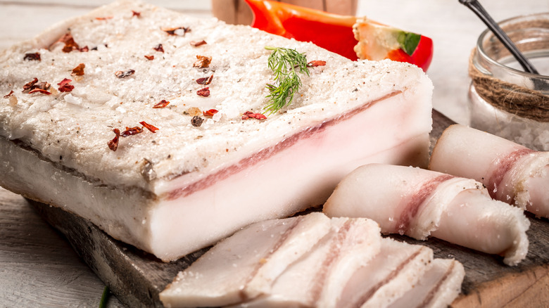 Block of lard with thin slices cut off on cutting board