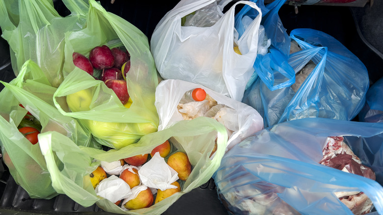 Plastic grocery bags full of food in the trunk of a car