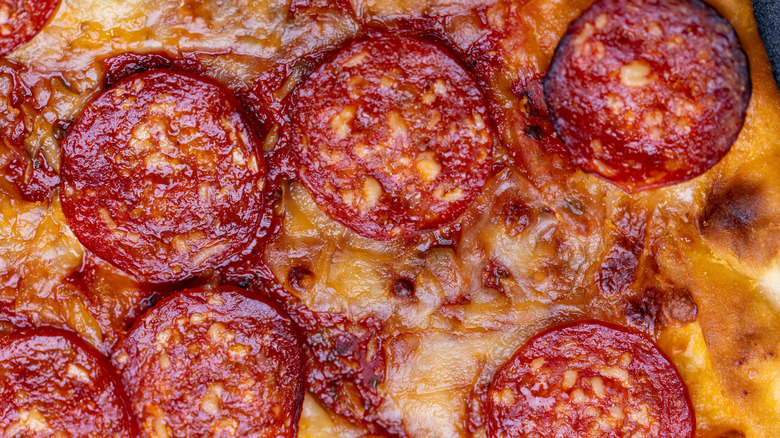Close up on a pepperoni pizza with glistening, crispy-edged pepperoni embedded in melted cheese