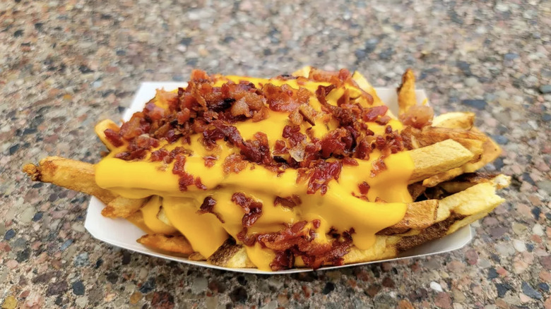 Fries topped with cheese in bacon in a paper container
