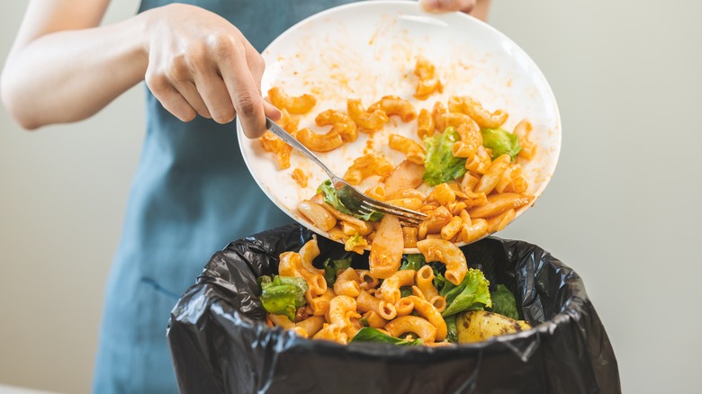 A person scrapes food scraps off a a plate into a garbage bin