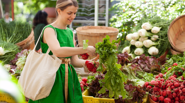woman in a green dress with a cloth shopping bag buying fresh produce at an Oregon farmers market