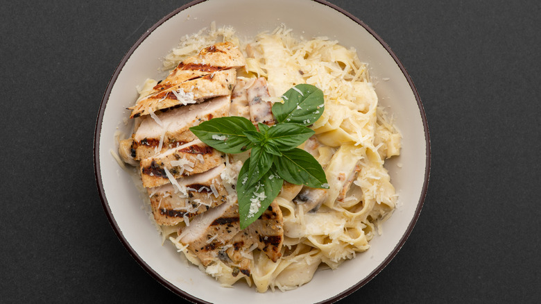 Chicken alfredo in white bowl with herbs