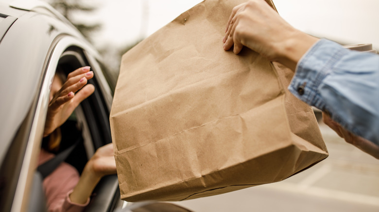 Person handing a brown takeout bag to a customer in their car