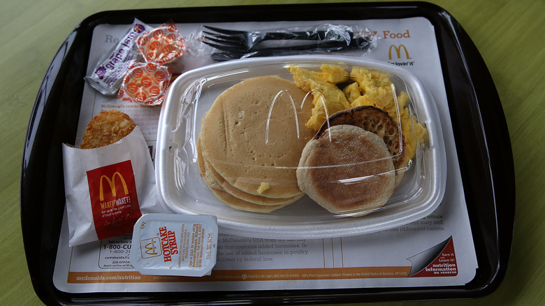McDonald's big breakfast with scrambled eggs, English muffin, hash brown, hotcakes, syrup, butter and jelly on a tray