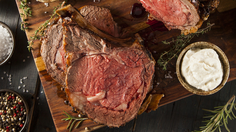 Overhead of prime rib on cutting board with cup of creamy horseradish sauce