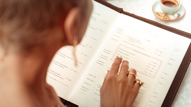 View over the shoulder of a person reading a restaurant menu with a small cup of coffee