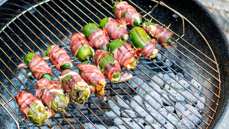 rows of bacon-wrapped jalapeño poppers on a charcoal grill