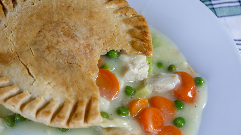 Chicken pot pie on a plate with veggies and meat coming out of it