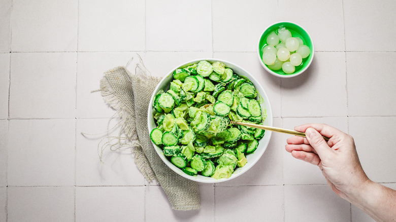 Hand lifting a forkful of avocado cucumber salad from bowl