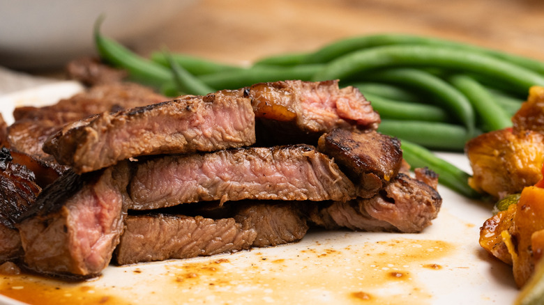 Stacks of saucy steak cut on plate next to green beans
