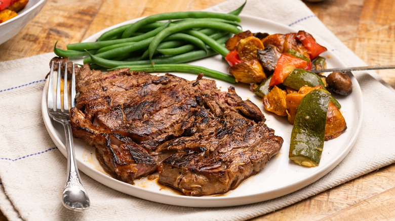 A plate of cooked steak with vegetables on top of a nakin