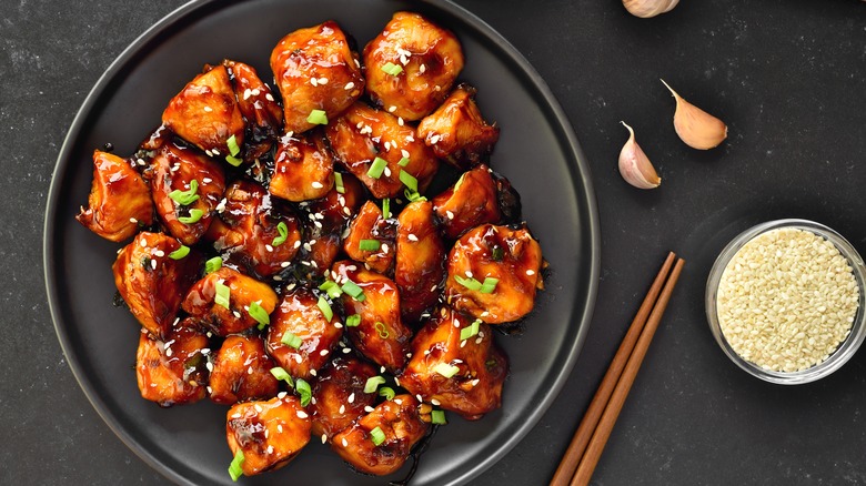 a plate of teriyaki chicken garnished with scallions and sesame seeds
