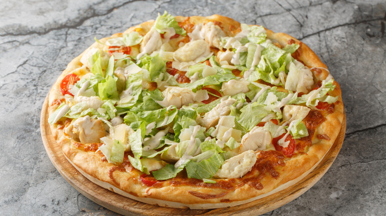 A homemade Caesar salad pizza topped with lettuce, chicken, and drizzles of sauce