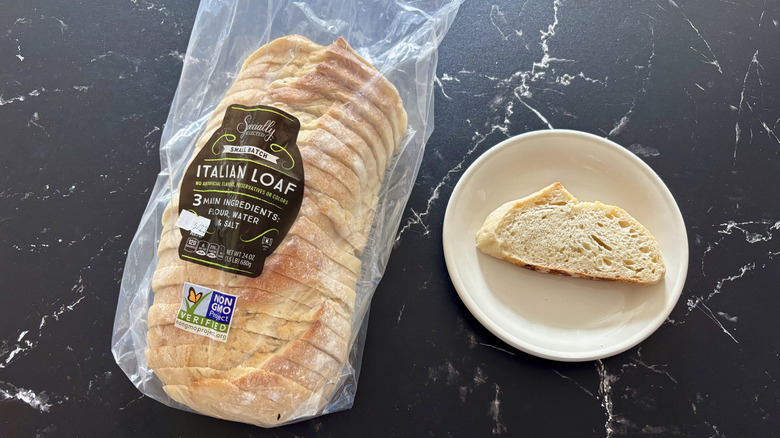 Aldi Specially Selected Italian Loaf presliced bread in plastic bag next to slice of bread on white plate atop dark marble surface