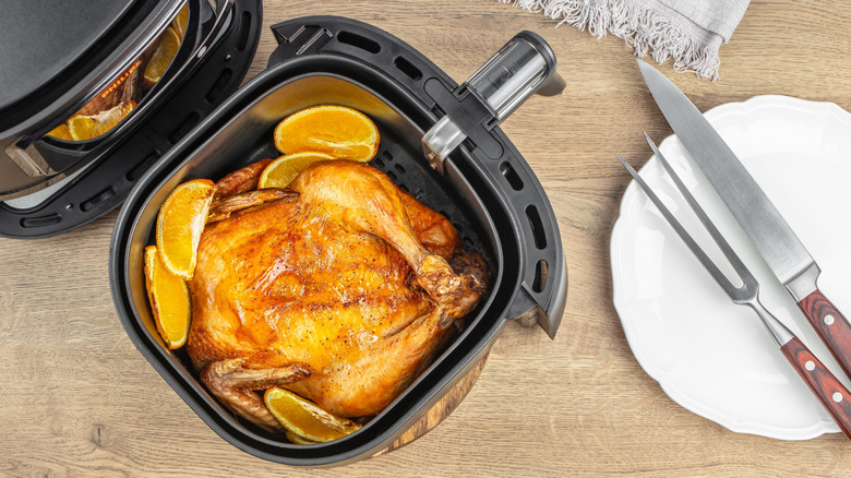 roasted chicken in an air fryer basket with plate and carving knife beside it