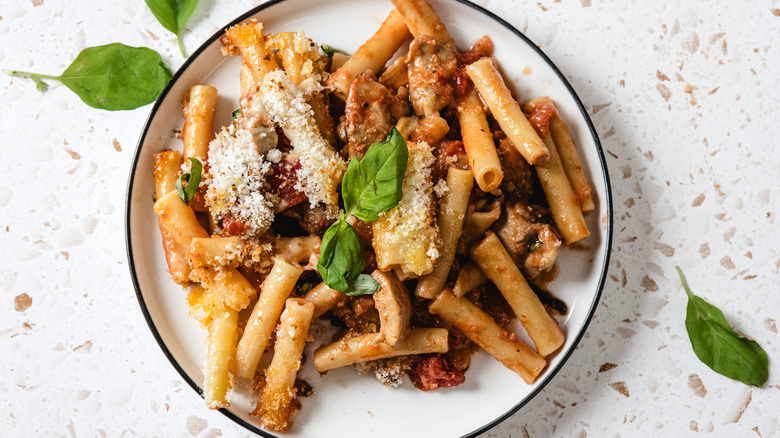 A baked ziti and chicken parm casserole topped with fresh basil on a white plate