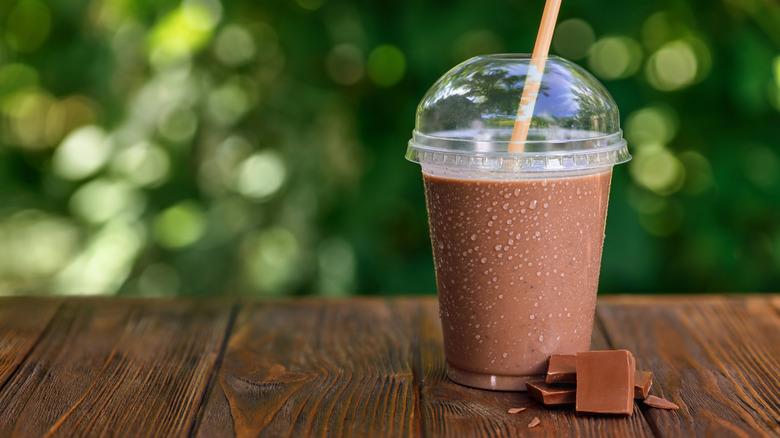 Chocolate milkshake in a takeaway glass on table, in front of green background