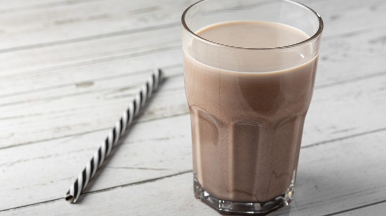 Chocolate milk in cup with black and white straw next to it