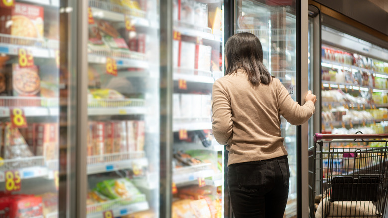 person shopping for a frozen meal in a grocery store fridge