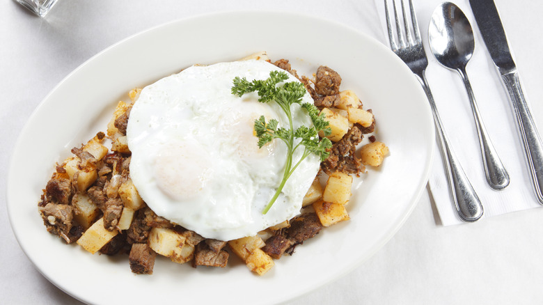 Top-view of homemade pot roast hash topped with fried eggs on a plate next to silverware