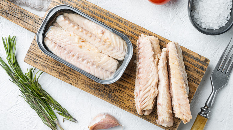 Mackerel filets in the can and on a wood board surrounded by rosemary and salt