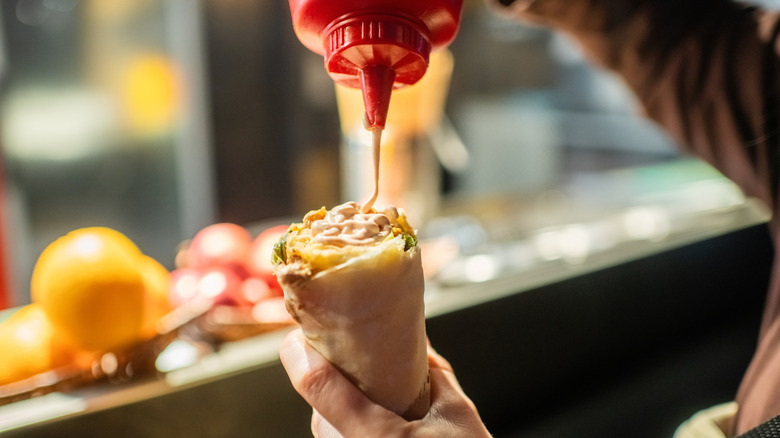 Hand drizzling bottle of sauce over chicken wrap