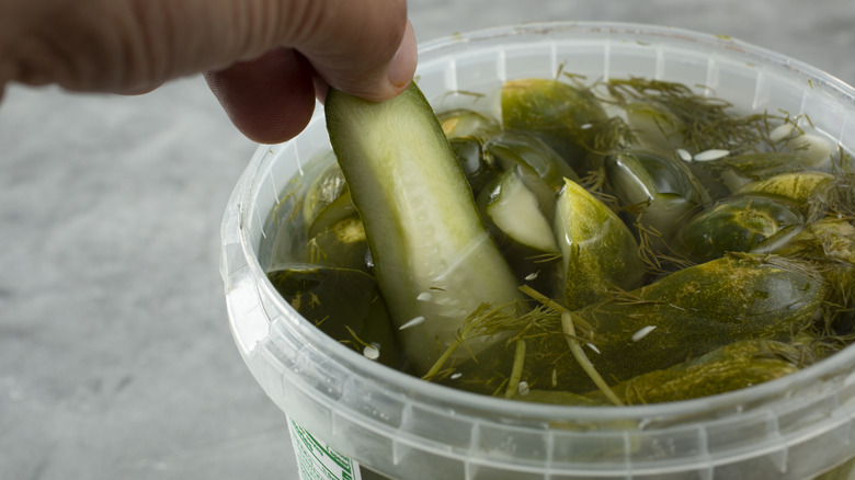 hand pulling a pickle spear out of a plastic container of pickles