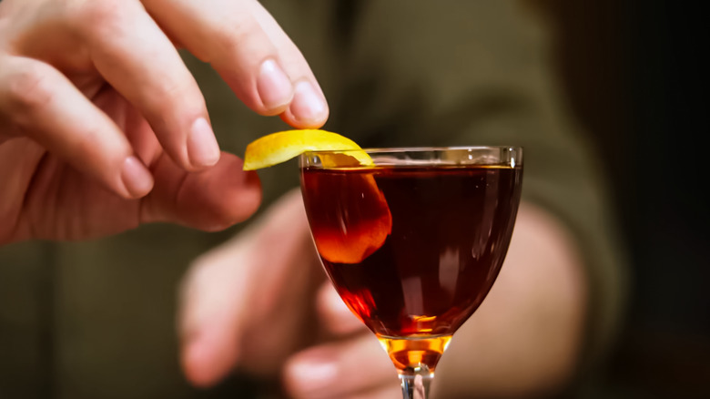 closeup of bartender putting orange twist garnish on red cocktail
