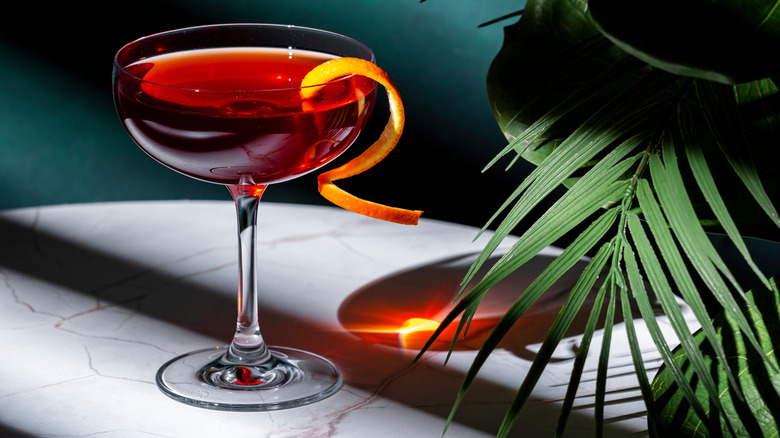 red deshler cocktail with orange twist on table with green leaf