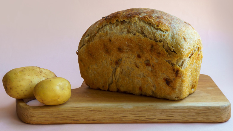 two potatoes and loaf of bread on wooden board