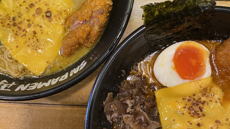 Two bowls of ramne with american cheese, jammy egs, mushrooms and fried chicken