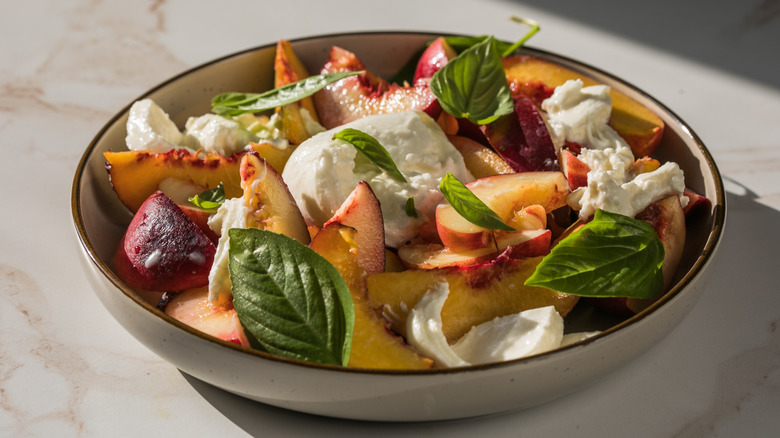 A plate of burrata is adorned with peaches and fresh basil leaves
