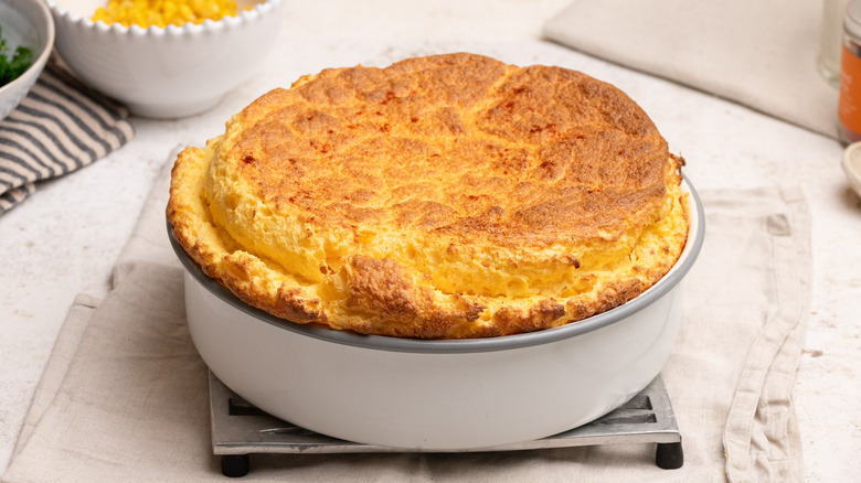 baked cheesy corn souffle in baking dish sitting on trivet over cloth