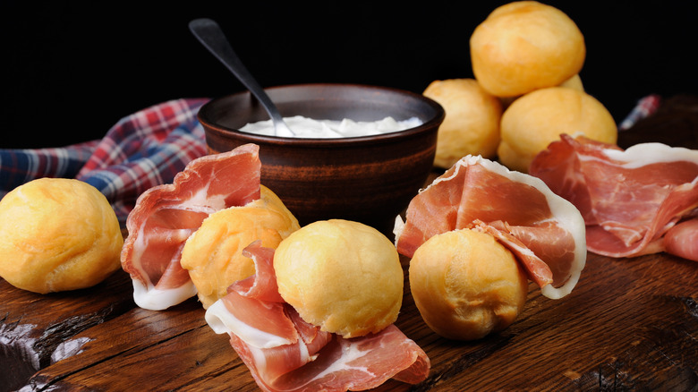 Coccoli and prosciutto on wood with bowl of cheese