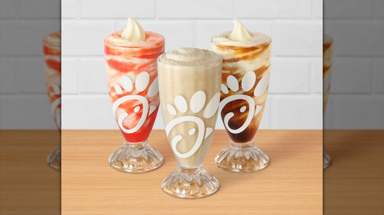 Plastic cups of frosted soda, soda float, and cola from Chick-fil-A sitting on wooden table
